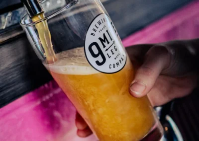 Close-up of a glass from 9 Mile Legacy Brewing Company being filled with light yellow beer from a tap