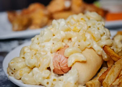 Close-up of a hot dog topped with mac and cheese, served with a side of thick-cut french fries