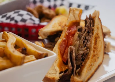 Close-up of a sliced roast beef sandwich on grilled bread with cheese and tomato, served with a side of thick-cut french fries