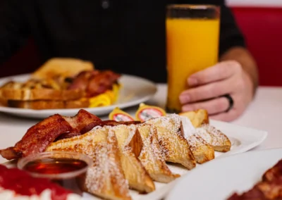 French toast and bacon breakfast with hand holding orange juice